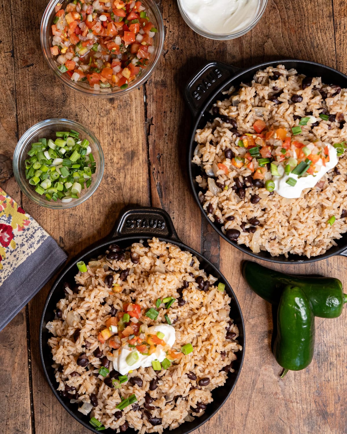 Two skillets of rice and black beans with fresh toppings