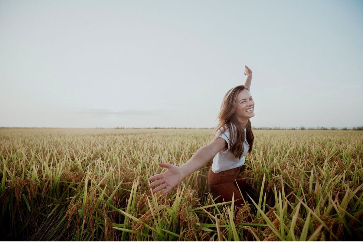 A young woman standing among the green stalks of a Louisiana rice field at harvest, arms outstretched and smiling